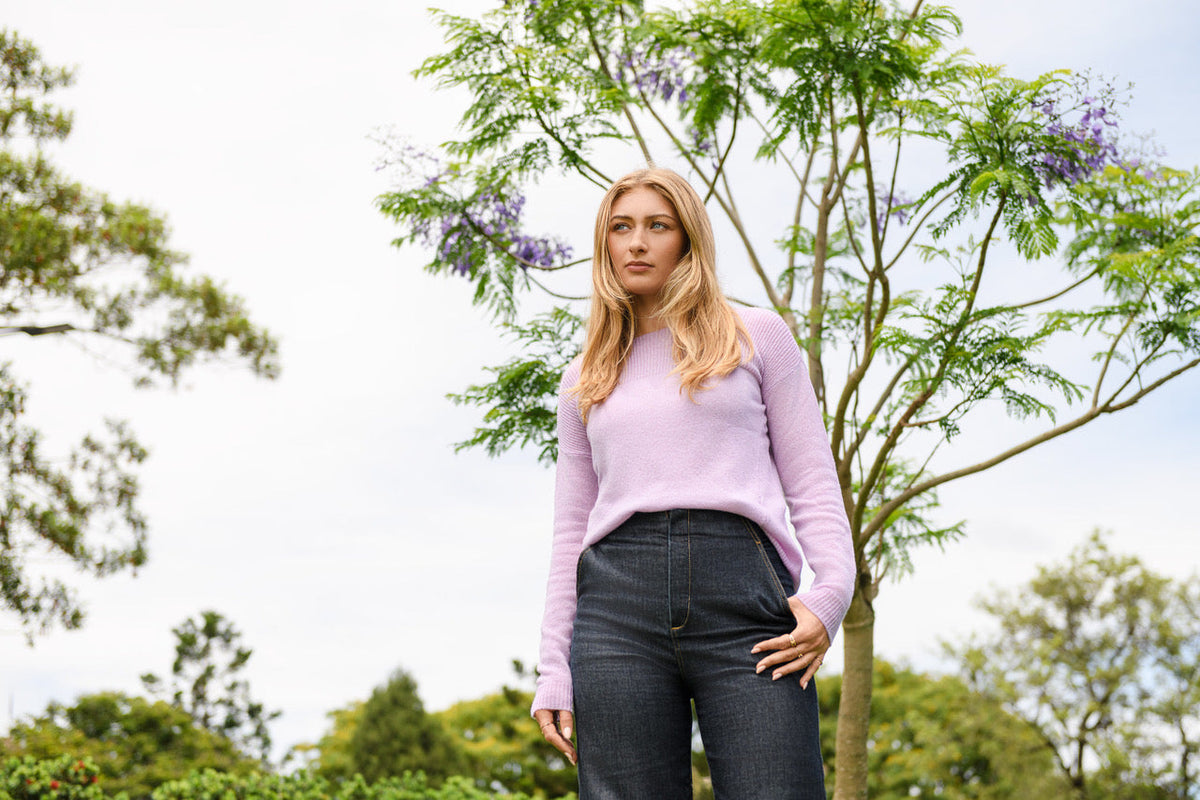NUAN Cashmere Lavender All Seasons Sweater worn with denim beneath a jacaranda tree in bloom